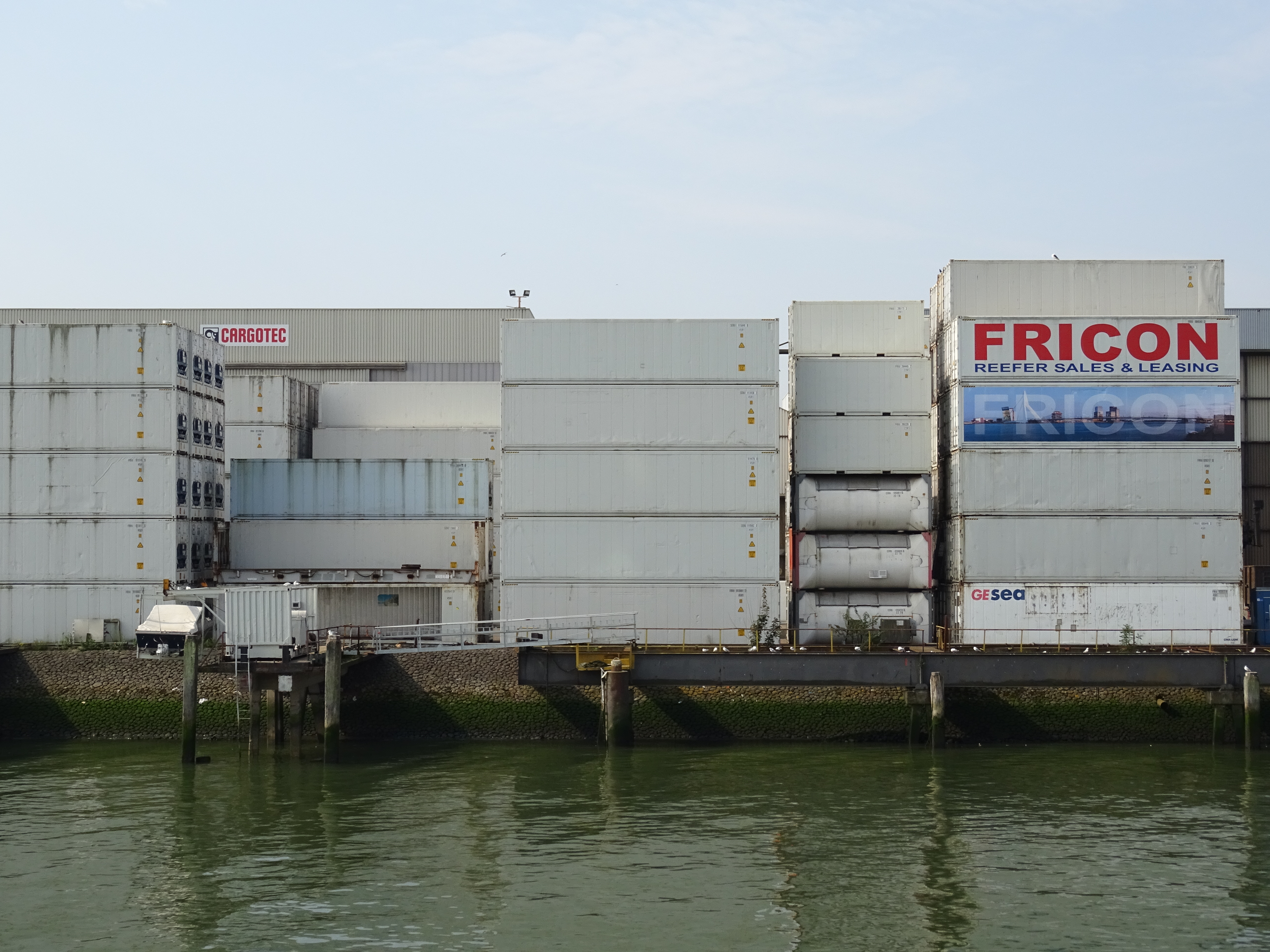 Stacked shipping containers at Port of Rotterdam — import tariffs add cost on top of gold's own price move