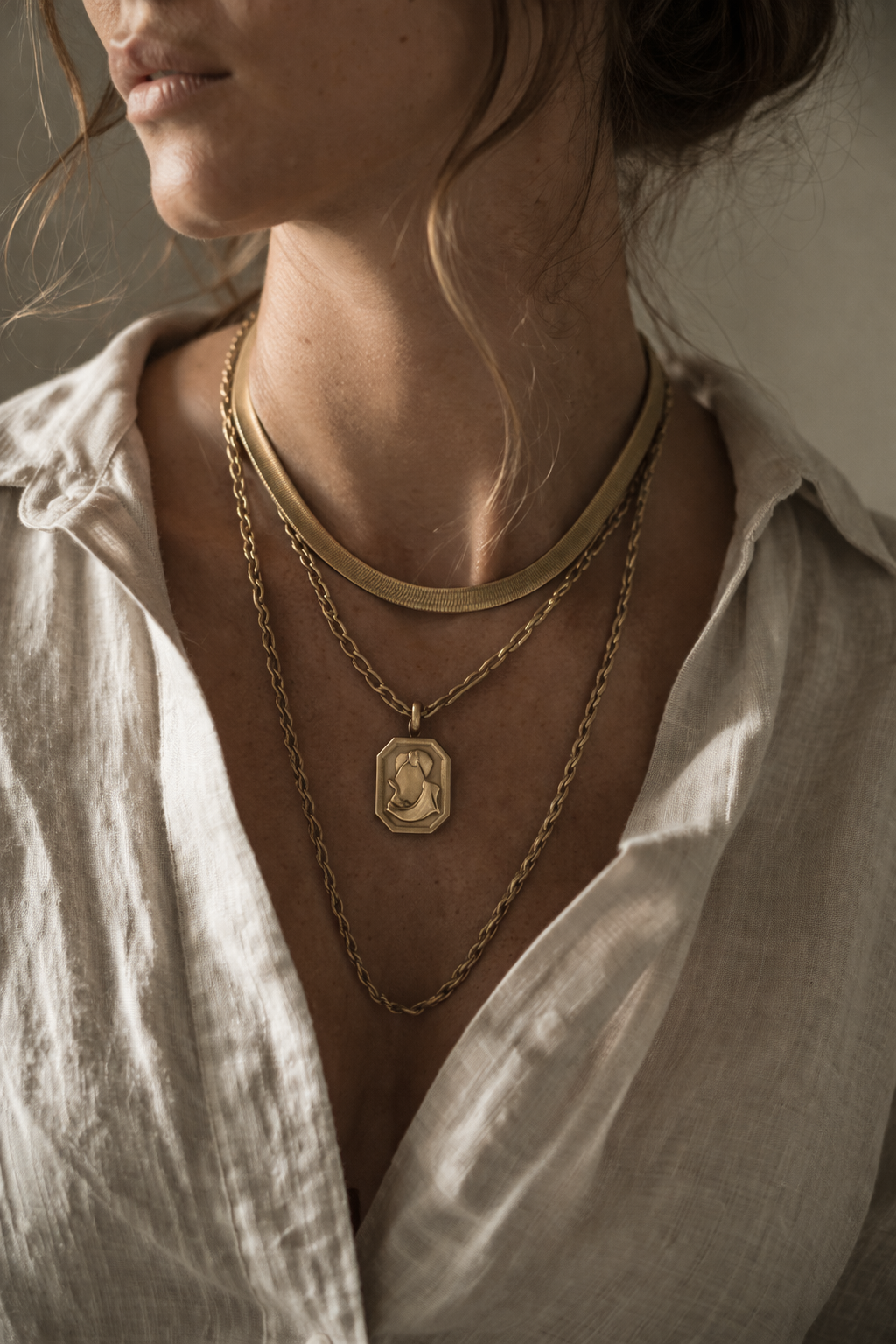Layered gold necklaces — herringbone chain, cable chain, and medallion pendant styled together