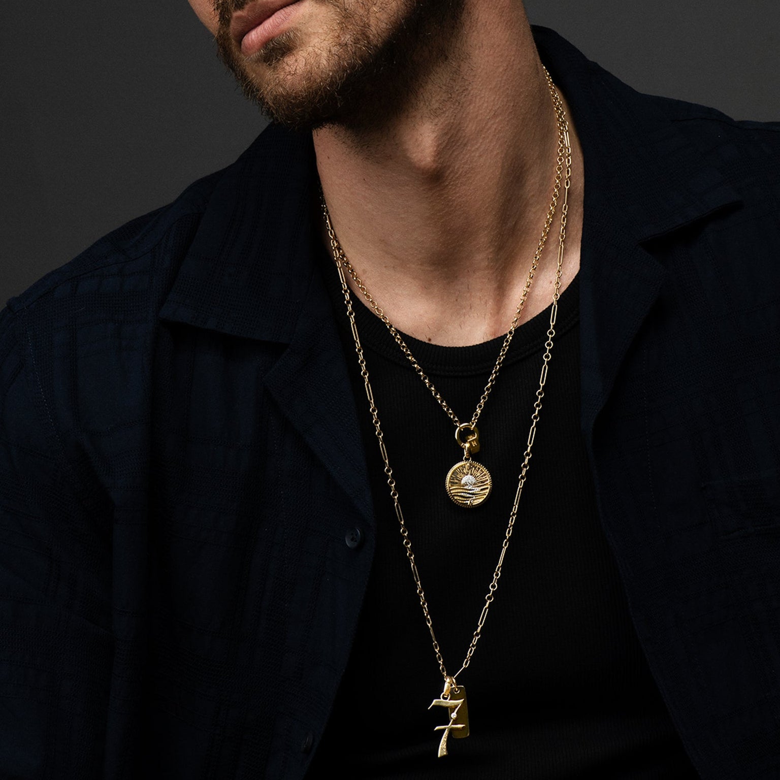 Man wearing layered Foundrae gold medallion chains and a round medallion pendant, dark open shirt